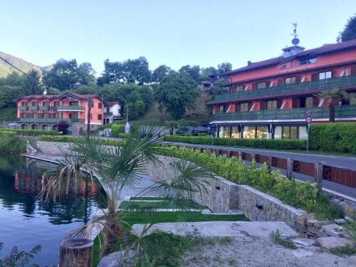 A serene lakeside resort with vibrant red buildings, lush greenery, and calm waters creates an inviting atmosphere for a tranquil getaway, ideal for travelers seeking relaxation and scenic beauty.