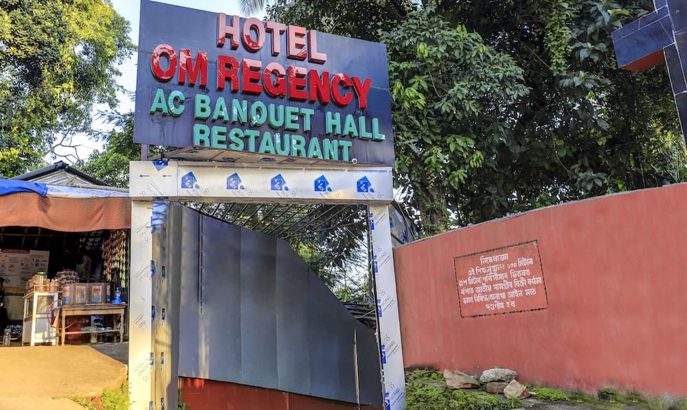 A vibrant entrance to Hotel Om Regency, featuring an AC Banquet Hall and Restaurant sign amidst lush greenery, offers travelers a welcoming and functional gateway for dining and event hosting.