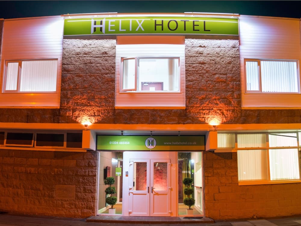 A warmly lit Helix Hotel entrance at night showcases a modern facade with stone accents, inviting travelers seeking comfortable accommodations.