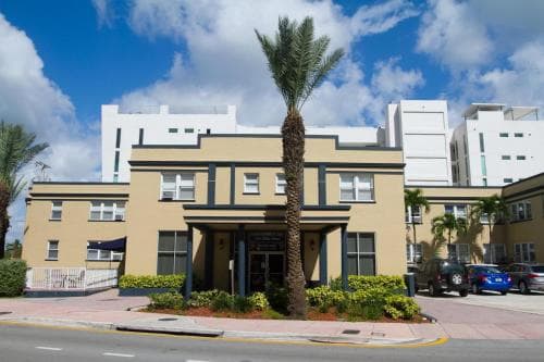 A sunny day highlights a charming, palm-fringed apartment building in an urban coastal area, ideal for travelers seeking a relaxed yet vibrant stay near modern amenities.