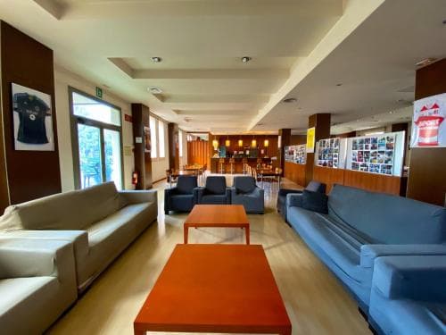 A cozy hotel lobby features modern sofas, vibrant orange tables, and framed jerseys on the walls, creating a welcoming atmosphere ideal for travelers seeking relaxation and comfort.