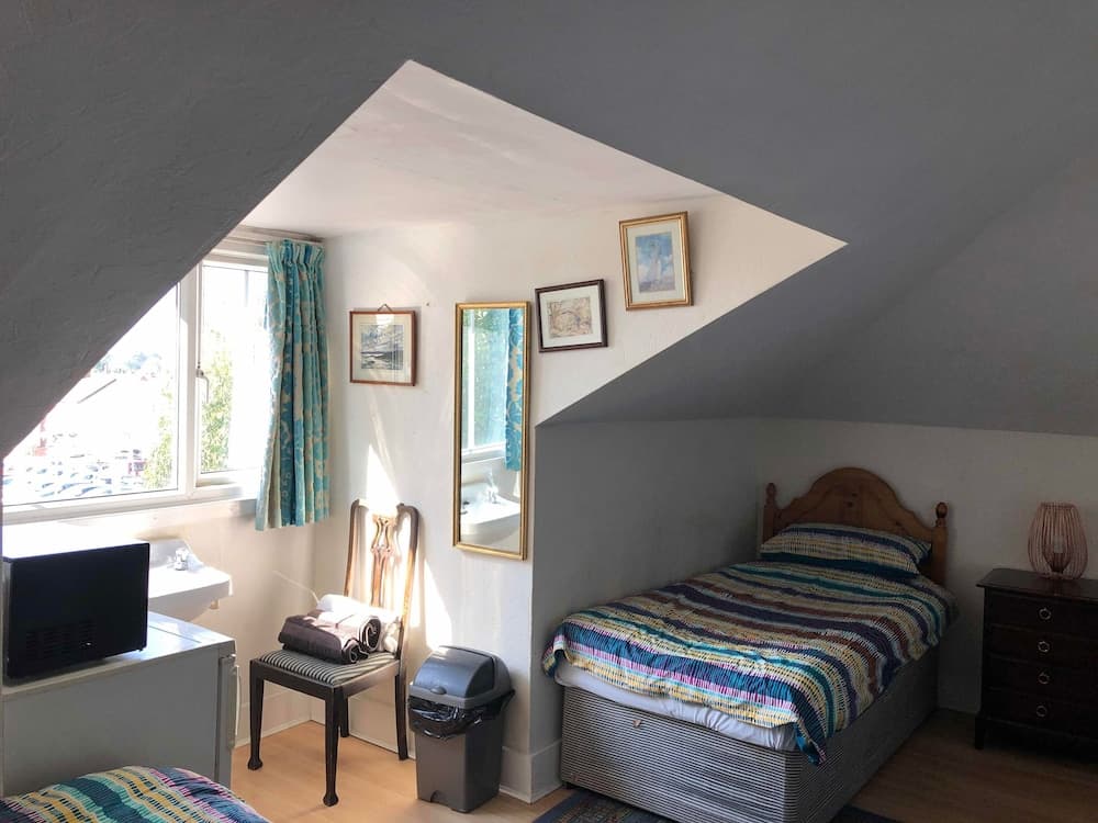 A cozy attic bedroom with slanted ceilings, a single bed adorned with a colorful striped blanket, framed artwork on the walls, and a window offering natural light, ideal for travelers seeking a quaint and comfortable stay.