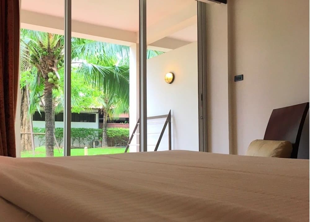 A serene bedroom with a neatly made bed overlooks lush tropical greenery through large glass doors, ideal for travelers seeking relaxation in a tranquil resort setting.