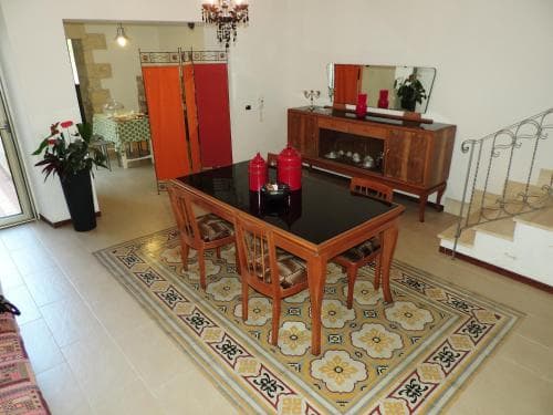 A cozy dining area with a wooden table set on a vibrant patterned rug, surrounded by warm-toned furniture and decorative elements, creates an inviting atmosphere ideal for travelers seeking a comfortable rental space.