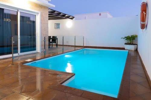 A serene evening at a private villa features a glowing pool surrounded by tiled flooring, modern glass doors, and minimalistic decor, ideal for travelers seeking relaxation and luxury accommodations.
