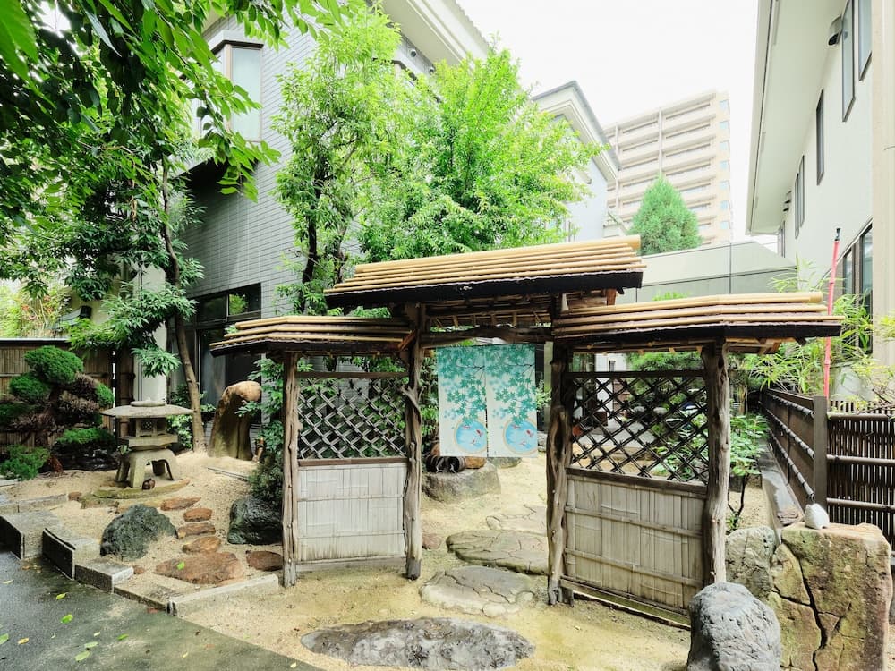 A serene urban oasis featuring traditional wooden gates, lush greenery, and stone pathways invites travelers to explore its tranquil Japanese garden ambiance, perfect for cultural immersion and relaxation.