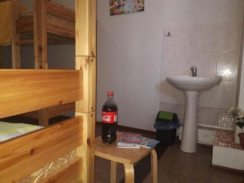 A cozy hostel room featuring wooden bunk beds, a small sink, and a Coca-Cola bottle on a table, ideal for budget travelers seeking a simple and functional accommodation.