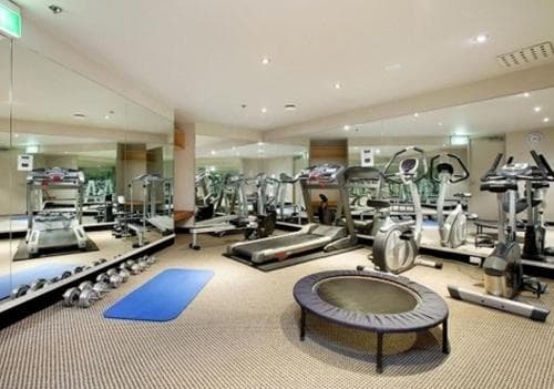 A well-lit indoor gym features an array of cardio machines, mirrored walls, and a trampoline, creating a modern and inviting space ideal for fitness enthusiasts seeking a comprehensive workout environment.