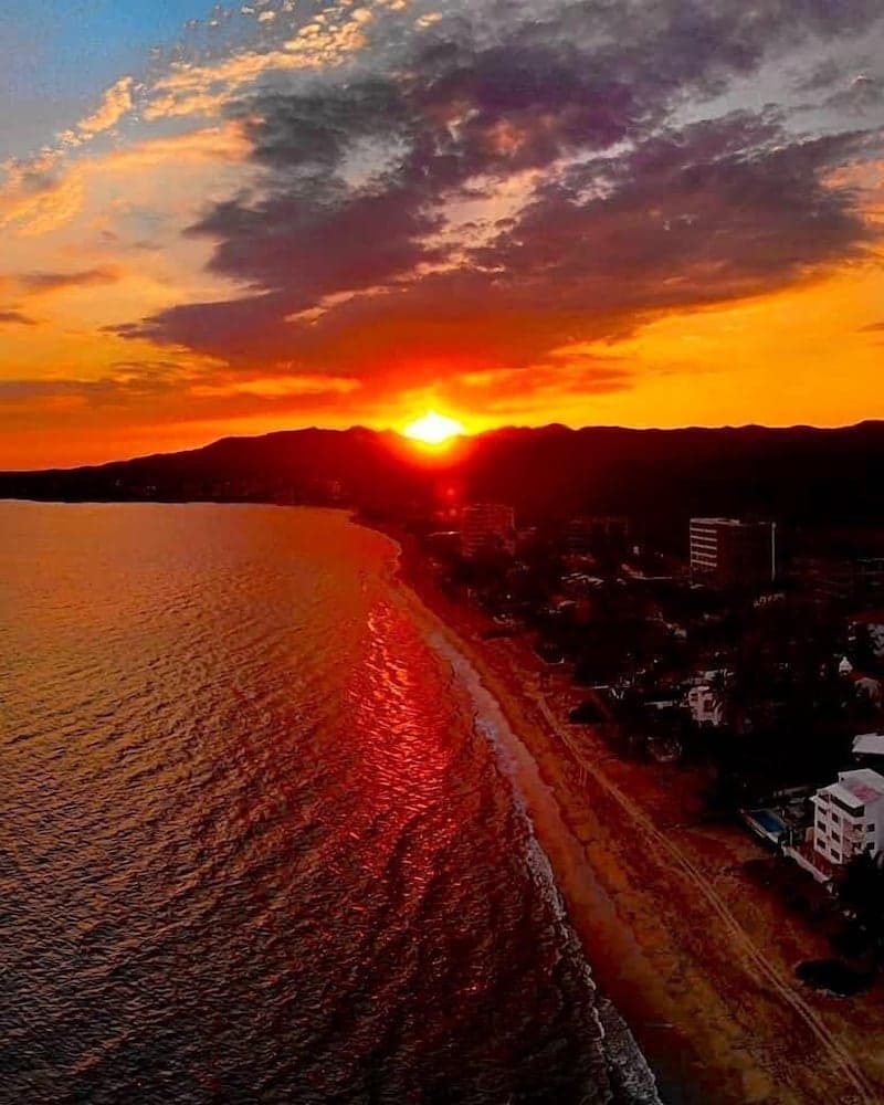 A breathtaking sunset casts vibrant orange hues over a coastal town beside calm waters, ideal for travelers seeking serene beachside relaxation and picturesque photography opportunities.