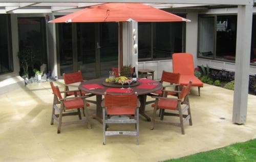 A cozy outdoor patio features a vibrant orange umbrella shading a round table set with colorful chairs, perfect for a relaxing dining experience in a serene residential setting.