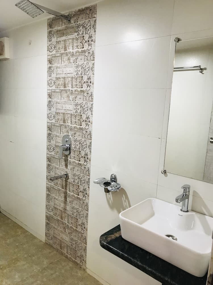 A clean and modern bathroom features a stylish tiled shower wall, a sleek sink with a granite countertop, and a large mirror, ideal for travelers seeking comfort and functionality in their accommodations.