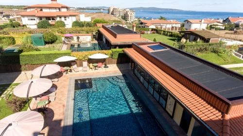 A serene coastal resort features a sparkling pool surrounded by lounge chairs under umbrellas, set against a backdrop of lush greenery and distant ocean views, ideal for a relaxing vacation getaway.