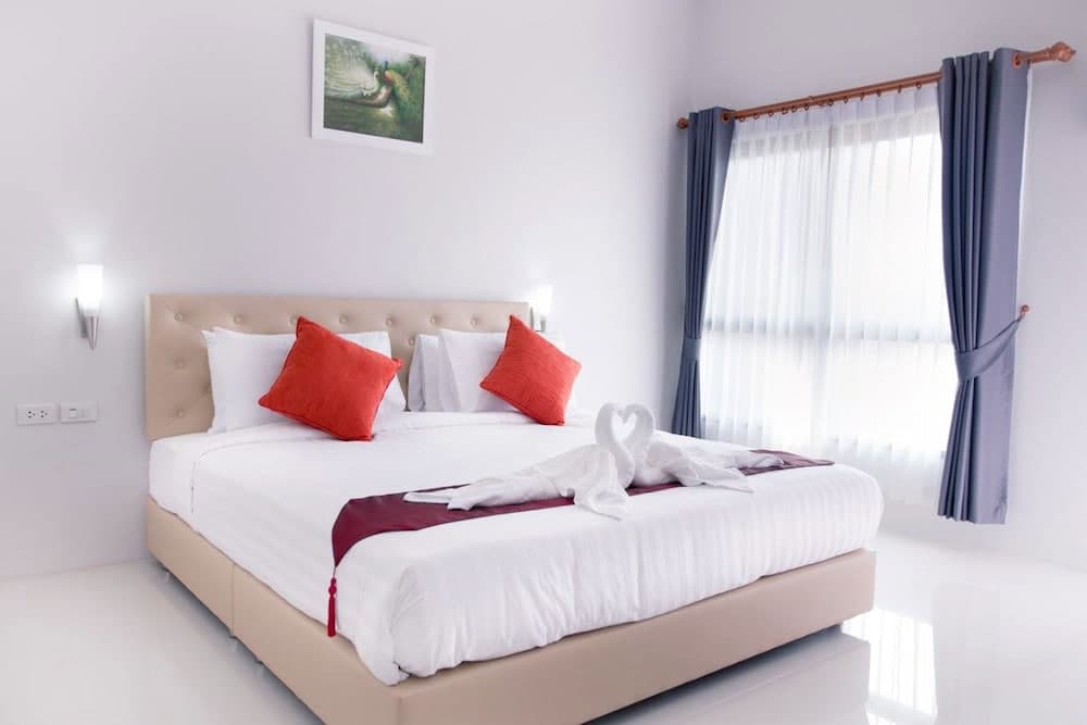A serene hotel bedroom features a cozy bed adorned with red pillows and towel art, framed by soft blue curtains and natural light, ideal for travelers seeking relaxation.
