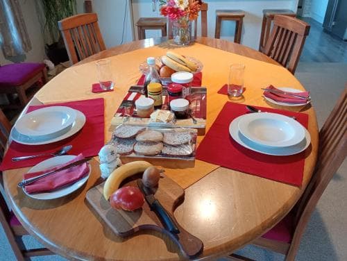 A cozy dining room table set for breakfast with fresh bread, fruit, and condiments, inviting travelers to enjoy a warm morning meal in a homely atmosphere.