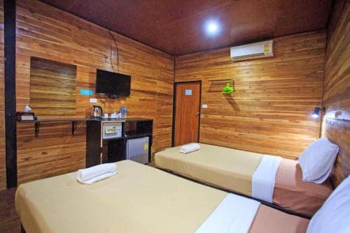 A cozy budget-friendly hotel room features wooden panel walls, two neatly made beds, a small fridge, and a mounted TV, ideal for travelers seeking comfort in a compact space.