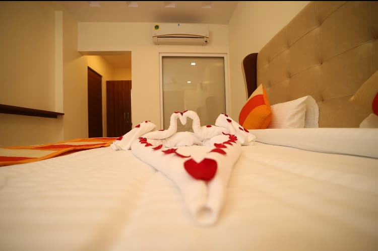 A cozy hotel room in Jaipur, Rajasthan, features a neatly made bed adorned with towel swans forming a heart, creating a romantic and inviting atmosphere ideal for travelers seeking comfort and charm.