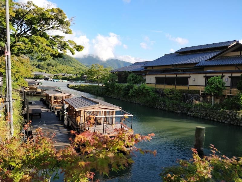 A serene riverside scene in Kyoto features traditional Japanese architecture, vibrant autumn foliage, and calm waters, ideal for tranquil cultural exploration and photography.