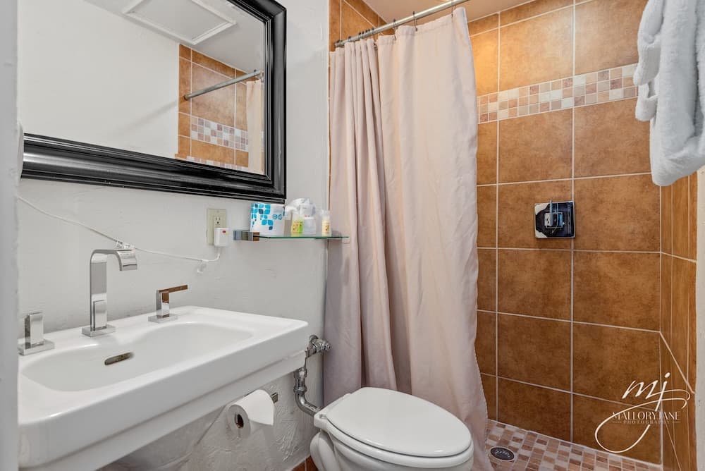 A cozy hotel bathroom features a white sink with dual faucets, a toilet, a beige shower curtain, and earth-toned tiled walls, creating a warm and inviting atmosphere ideal for travelers seeking comfort.