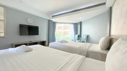 A cozy hotel room with two neatly made beds, a flat-screen TV, and a balcony view of outdoor seating, ideal for travelers seeking comfort and relaxation.
