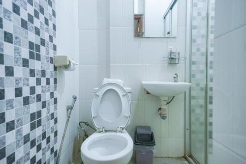 A clean, compact bathroom with checkered tiles, a toilet, sink, and shower area offers a practical space for travelers seeking basic amenities in budget accommodations.