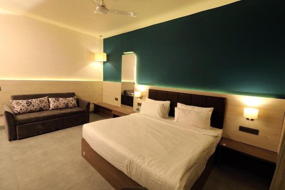 A cozy hotel room features a neatly made bed with white linens, a green accent wall, warm lighting, and a comfortable sofa, ideal for travelers seeking relaxation and comfort.