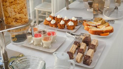 A cozy breakfast buffet scene featuring assorted pastries, cereal dispensers, and neatly arranged desserts on white trays, ideal for travelers seeking a comfortable morning start in a hotel setting.
