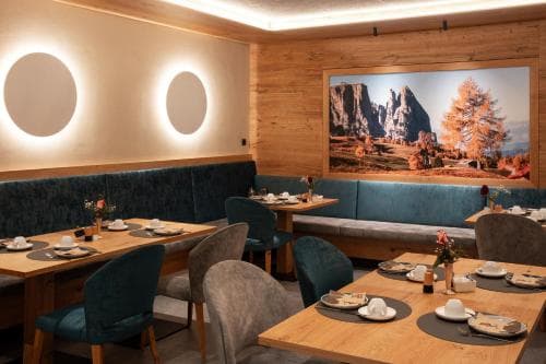 A cozy restaurant with wooden walls, plush teal seating, and a large scenic mountain mural creates an inviting atmosphere perfect for travelers seeking a warm dining experience in a rustic setting.