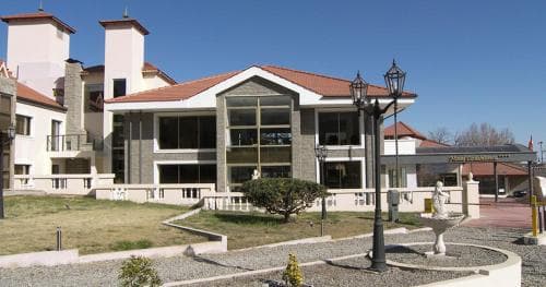 A serene courtyard with a fountain, lampposts, and lush greenery in front of a modern building under a clear blue sky, ideal for a tranquil business retreat or conference setting.