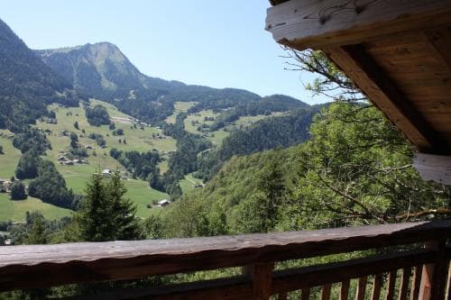 A serene mountain valley view from a wooden balcony offers a tranquil escape, ideal for nature lovers seeking peaceful retreats amidst lush greenery and rolling hills.