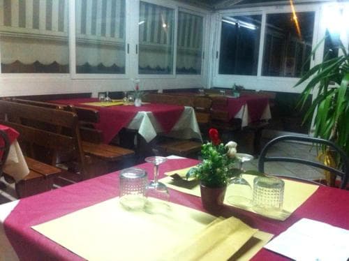 A cozy indoor dining area with wooden tables draped in red tablecloths, set with glassware and floral centerpieces, evokes a warm and inviting atmosphere ideal for travelers seeking a comfortable restaurant experience.