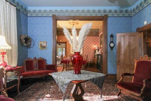 A cozy, vintage living room with blue patterned walls, ornate furniture, and a striking red vase on a central table invites travelers seeking a charming, historical accommodation experience.