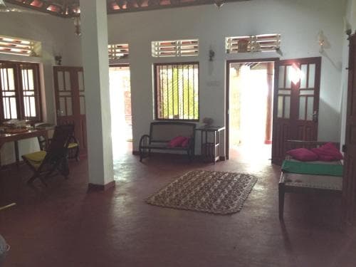 A cozy, open-concept living space with wooden furniture, vibrant cushions, and large windows invites travelers seeking a tranquil retreat in a homely villa setting.