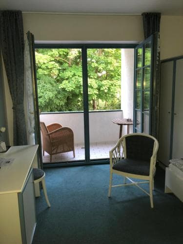A cozy hotel room with a balcony overlooking lush greenery, featuring comfortable seating and a serene atmosphere, ideal for travelers seeking relaxation and a connection to nature.