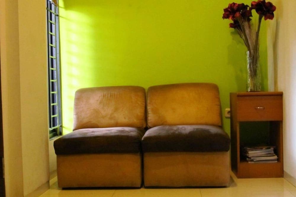 A cozy indoor seating area features two brown armchairs against a vibrant green wall, complemented by a wooden side table with a vase of red flowers, ideal for travelers seeking a comfortable and inviting rest spot.