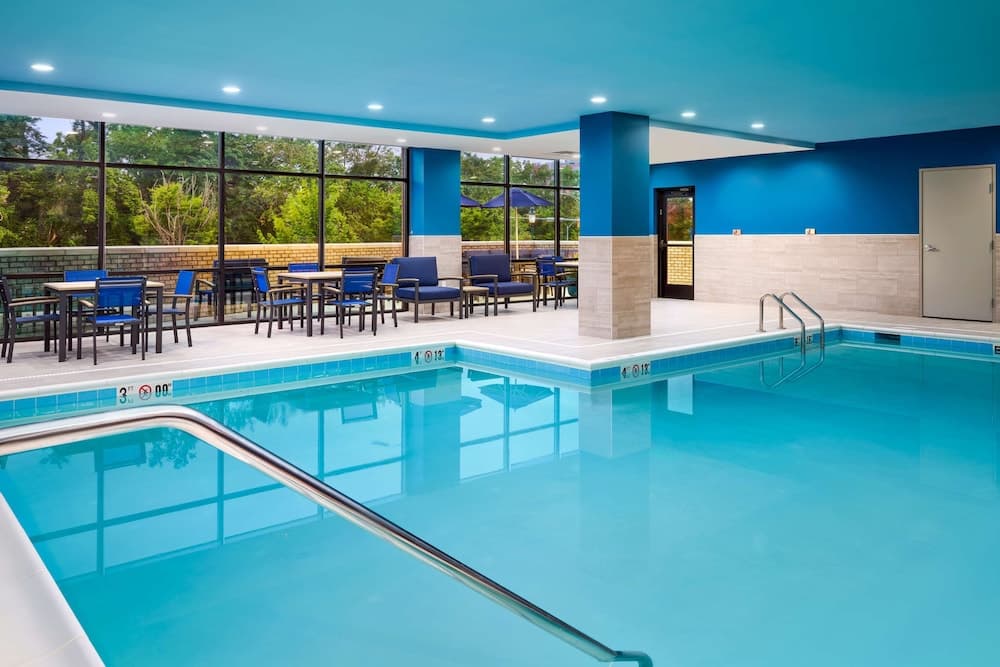 A serene indoor pool area with vibrant blue walls and ceiling, featuring lounge chairs, tables, and large windows overlooking greenery, ideal for relaxation and leisure activities at a resort or hotel.