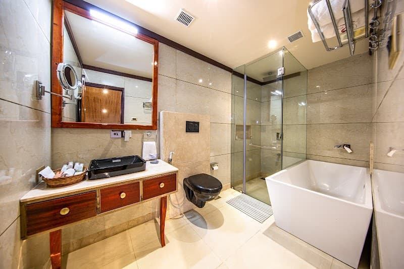 A luxurious bathroom at an upscale resort features elegant marble tiles, a modern bathtub, a glass-enclosed shower, and a wooden vanity, creating a serene and inviting atmosphere ideal for travelers seeking relaxation and comfort.