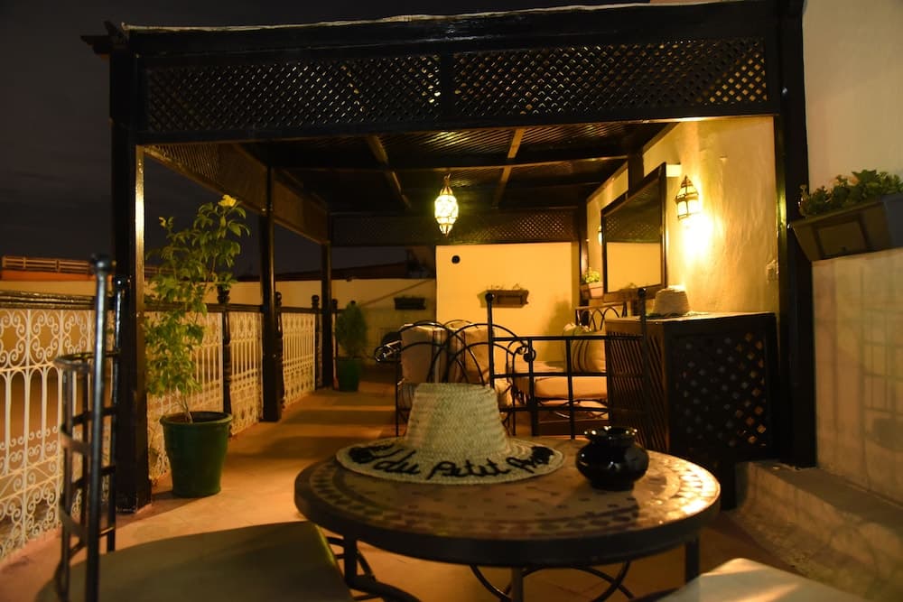 A cozy rooftop terrace at night, featuring warm lighting, a decorative pergola, potted plants, and inviting seating, creates an intimate ambiance perfect for travelers seeking a serene evening retreat.