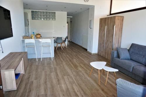 A cozy modern apartment features an open-plan living space with wooden flooring, sleek furniture, and a kitchen bar, ideal for travelers seeking comfort and convenience in urban accommodations.