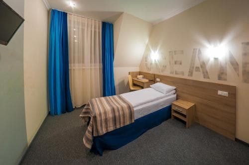 A cozy hotel room features a neatly made bed with blue accents, wooden furnishings, and a wall-mounted light display, ideal for travelers seeking comfort and simplicity.