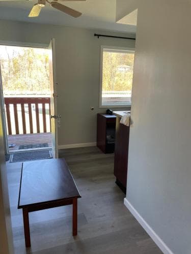 A cozy, minimalist room with light gray walls, wooden flooring, a simple table, and a view of autumn trees through an open sliding door, ideal for travelers seeking a peaceful retreat in a cabin or small apartment setting.