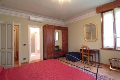 A cozy bedroom with a red bedspread, wooden wardrobe, and desk by the window, exuding warmth and comfort, ideal for travelers seeking a charming accommodation experience.