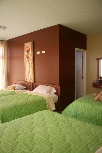 A cozy hotel room features two inviting beds with green quilts, a warm-toned wall with decorative art, and a private bathroom entrance, ideal for travelers seeking comfort and relaxation.