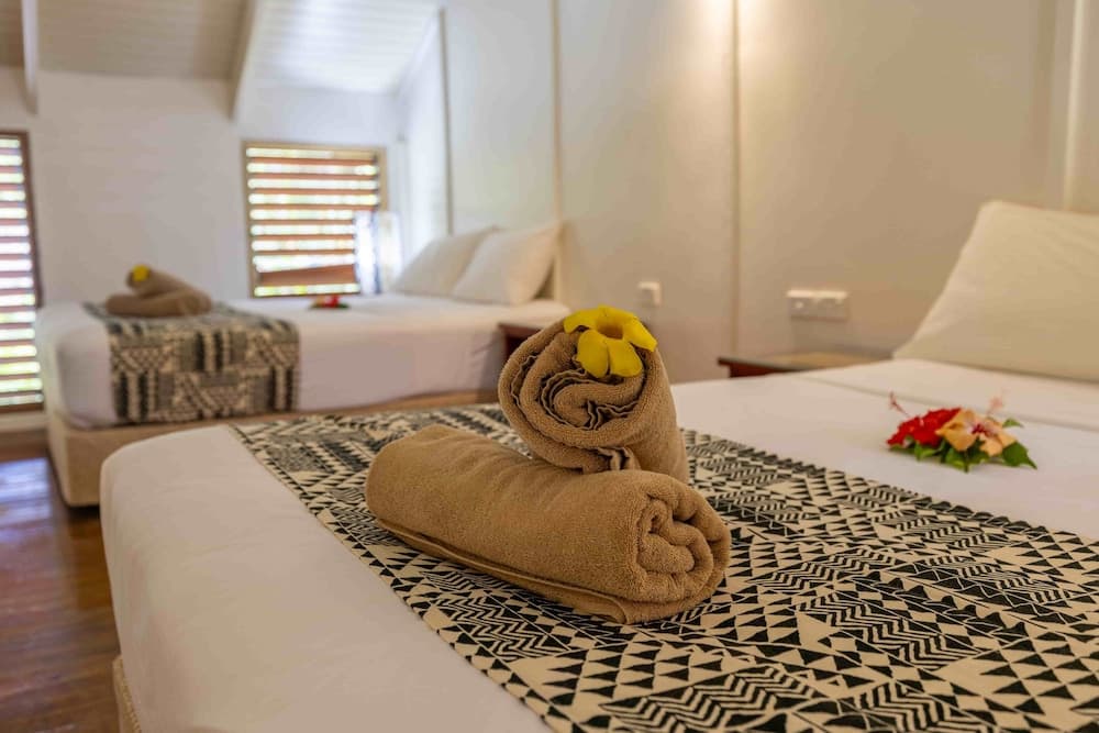 A cozy hotel room with neatly arranged beds adorned with patterned throws, decorative towels, and vibrant flowers, evokes a serene and inviting atmosphere ideal for travelers seeking relaxation.