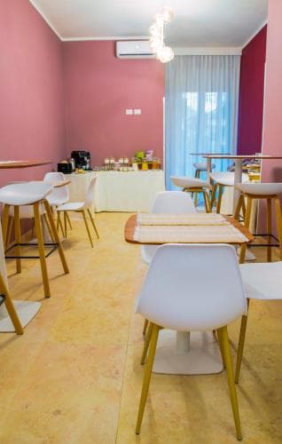 A cozy café with vibrant pink walls, modern white chairs, and wooden tables creates an inviting atmosphere perfect for travelers seeking a relaxing spot to enjoy refreshments.