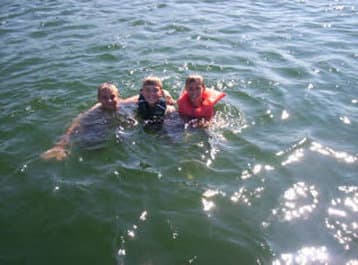 Three people enjoying a sunny day in the water, wearing life jackets, perfect for family-friendly beach activities and summer vacation memories.