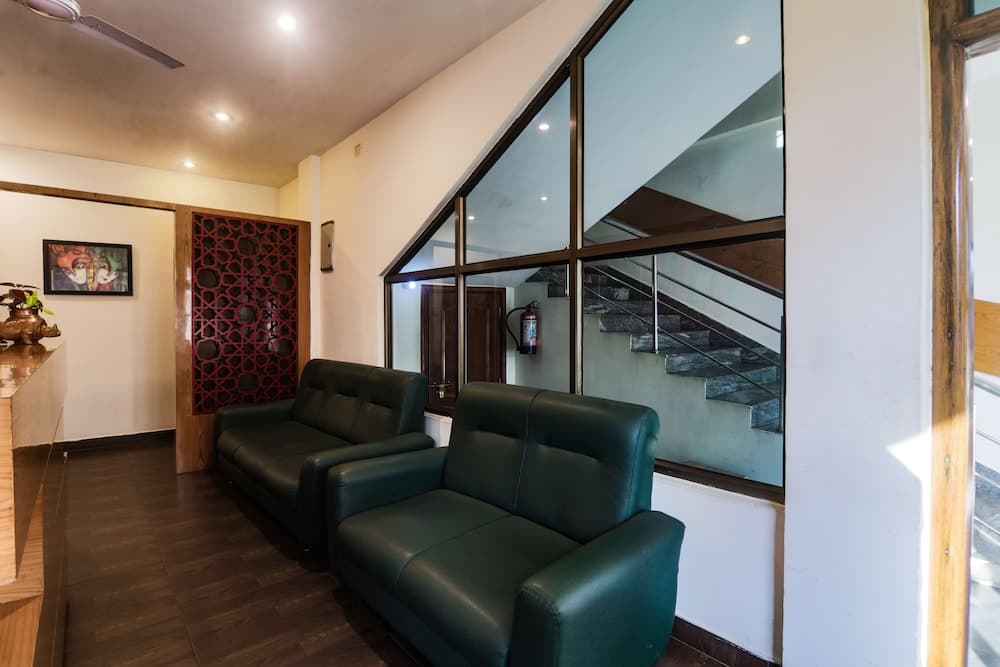 A cozy hotel lobby features plush green leather sofas, a stylish glass-enclosed staircase, and warm wooden accents, creating an inviting atmosphere ideal for travelers seeking comfort and relaxation.