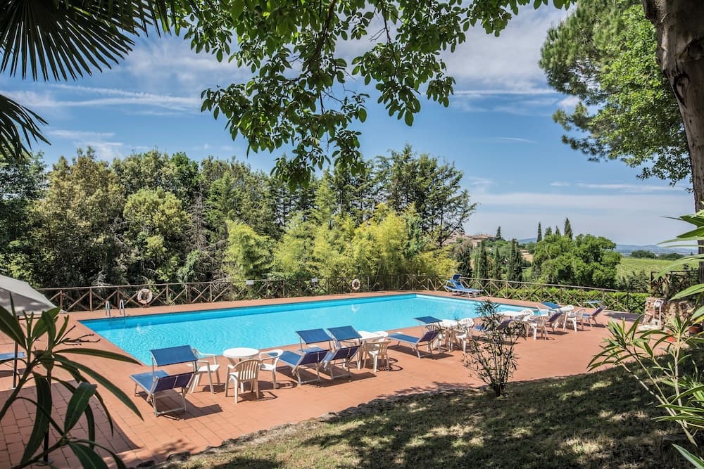 A serene outdoor pool area surrounded by lush greenery offers a tranquil retreat with lounge chairs and tables, perfect for relaxation and leisurely stays in a picturesque natural setting.