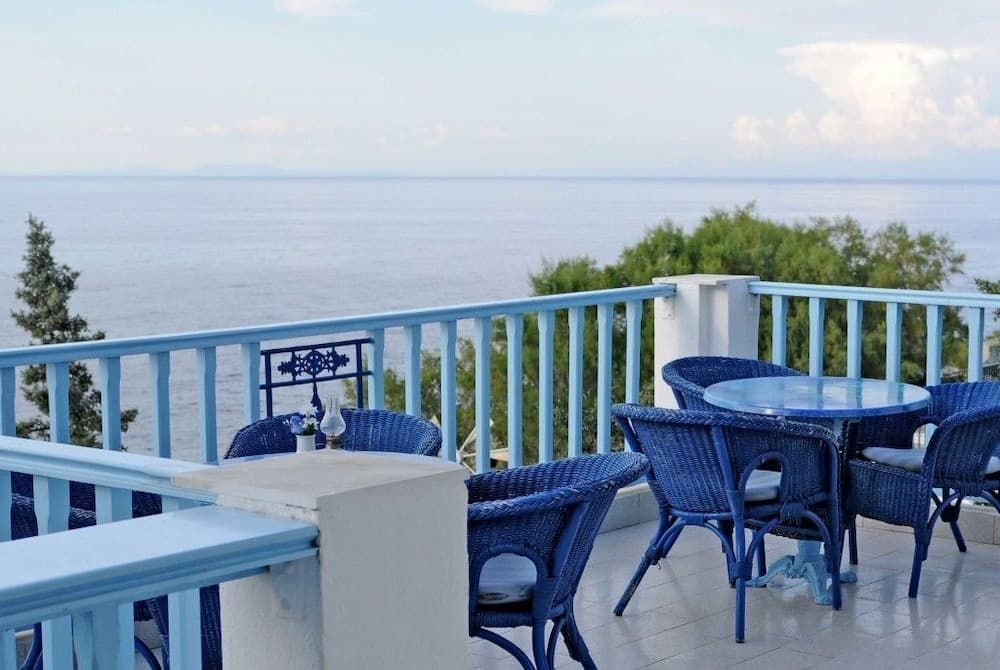 A serene seaside terrace features blue wicker furniture against a tranquil ocean backdrop, ideal for relaxing getaways and scenic dining experiences.