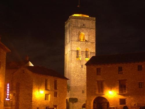 A warmly lit medieval tower stands tall against the night sky in a quaint European village, creating an enchanting atmosphere perfect for a romantic getaway or history-themed travel adventure.