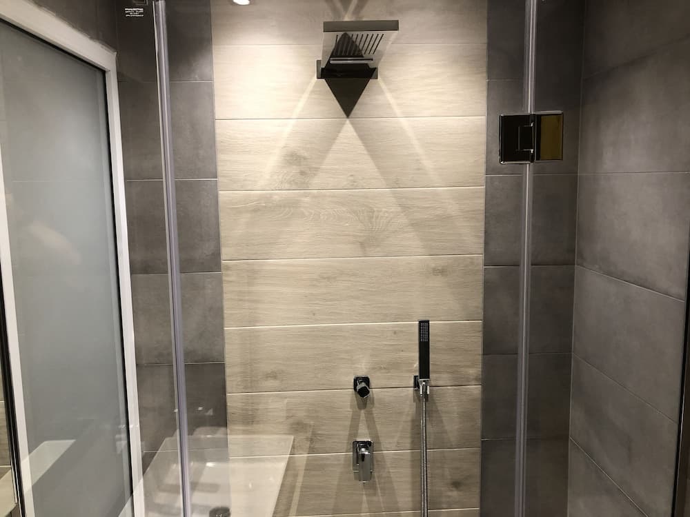 A modern shower enclosure featuring sleek gray tiles, wood-textured accents, and contemporary fixtures creates a serene and luxurious bathroom atmosphere ideal for home renovation inspiration.